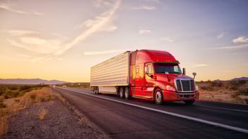 Large semi truck hauling freight on the open highway in the western USA under an evening sky.
