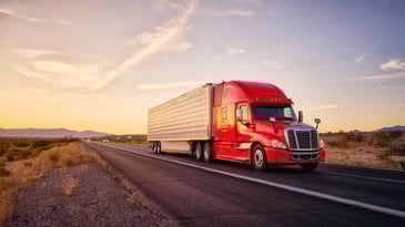Large semi truck hauling freight on the open highway in the western USA under an evening sky.
